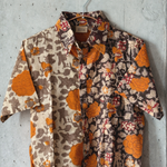 Orange and grey floral patterned shirt hanging on a hanger against a concrete wall.