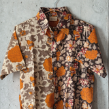 Orange and grey floral patterned shirt hanging on a hanger against a concrete wall.