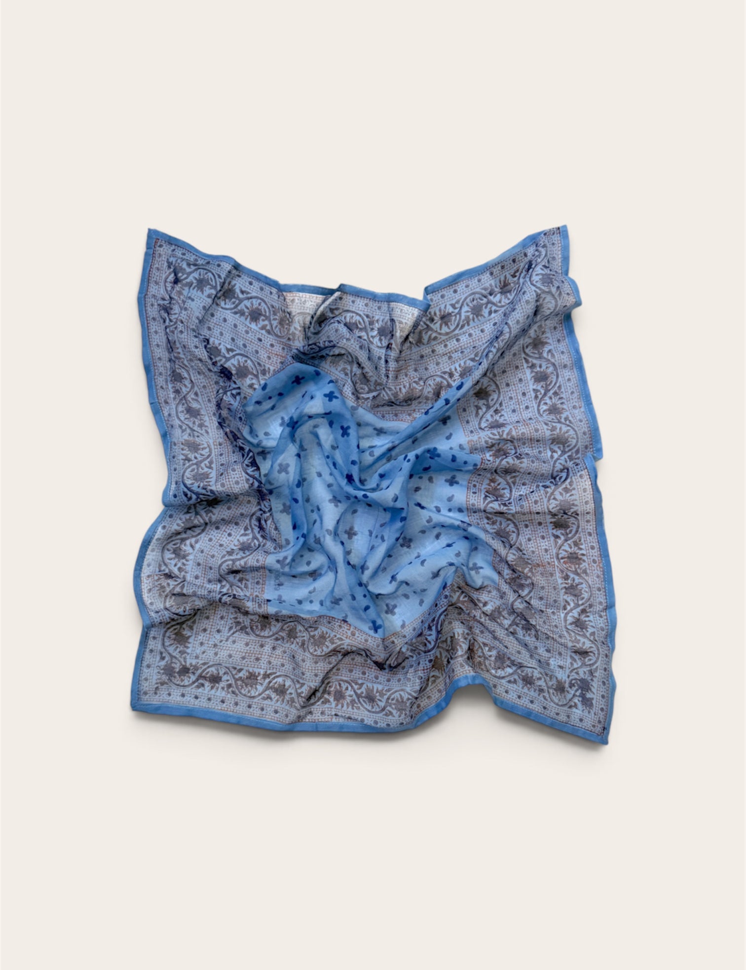 A square scarf with a blue and gray paisley pattern, laid flat on a light beige background.