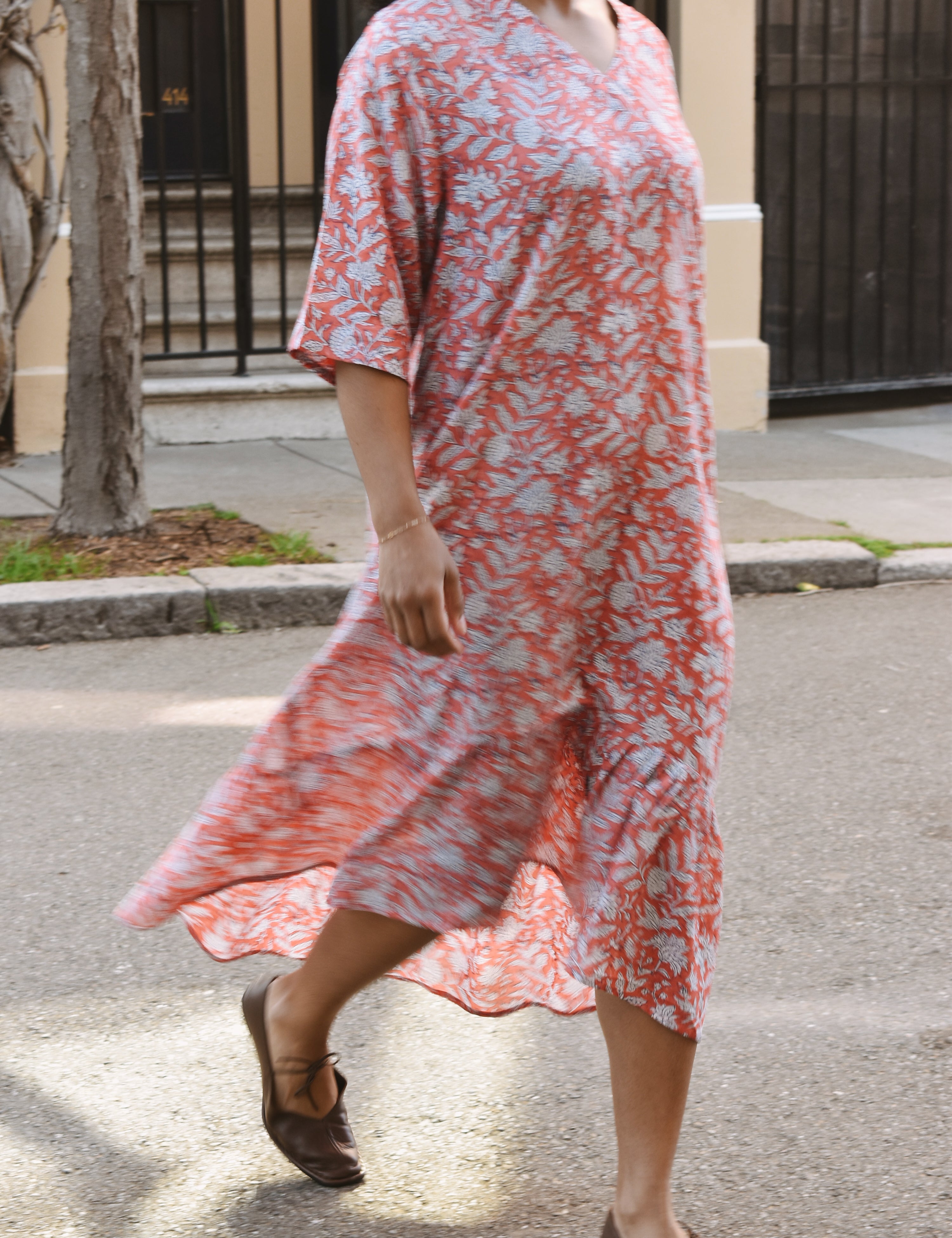 Woman in a pink and white floral dress walking on a street.