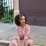 Woman in a pink floral dress sitting on a sidewalk next to a building.