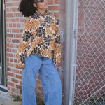 Person wearing a floral corduroy shirt and blue jeans leaning against a brick wall.