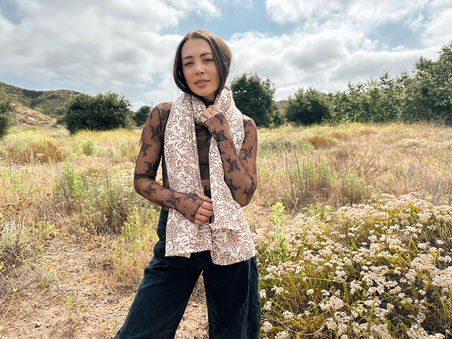 Block printed floral printed chunky wool scarf wrapped around neck, styled with sheer brown long sleeve and black denim jeans