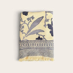 A folded waffle weave bath towel with a cream background and navy blue botanical and geometric patterns, featuring a fringed edge, shown against a solid off-white background.