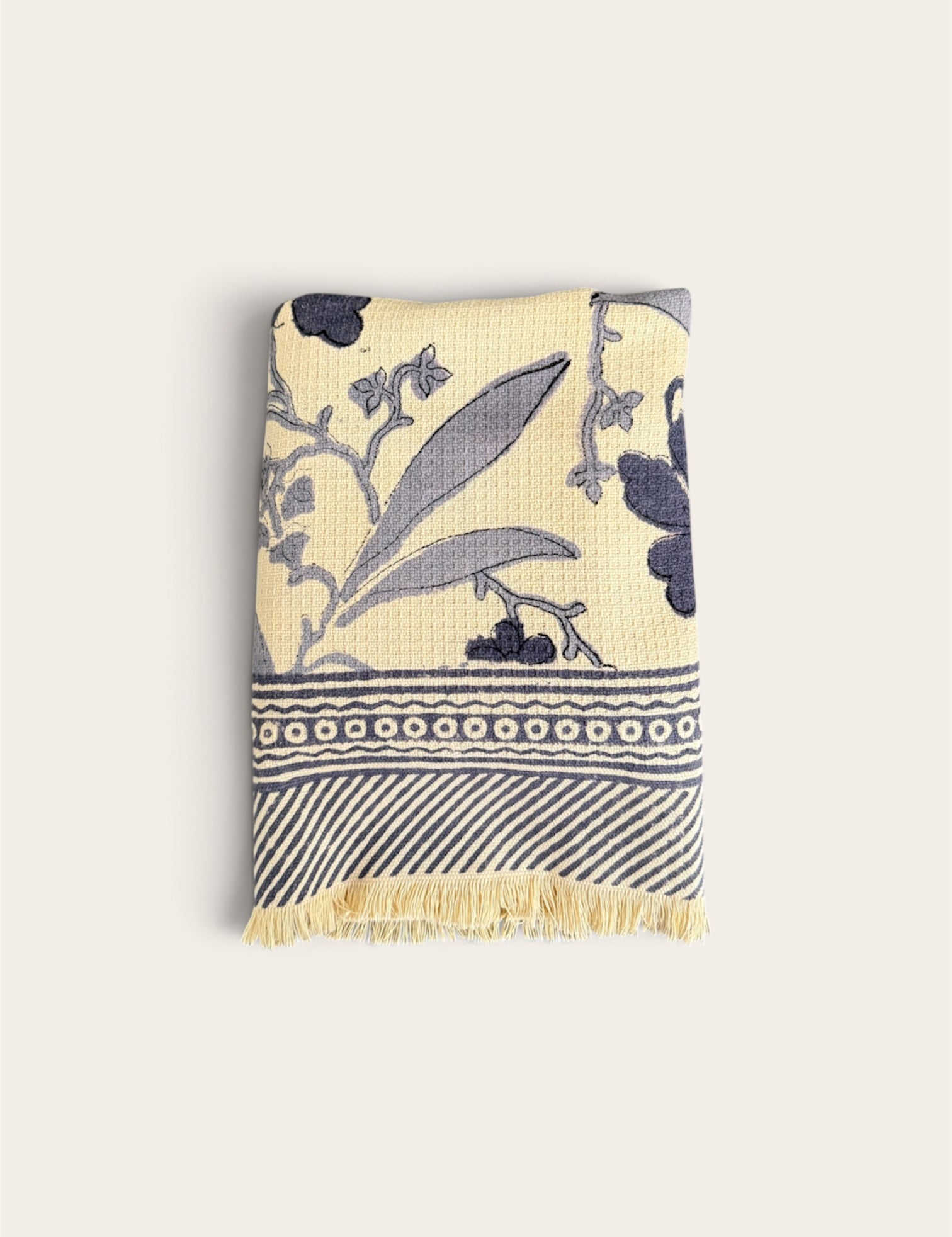 A folded waffle weave bath towel with a cream background and navy blue botanical and geometric patterns, featuring a fringed edge, shown against a solid off-white background.