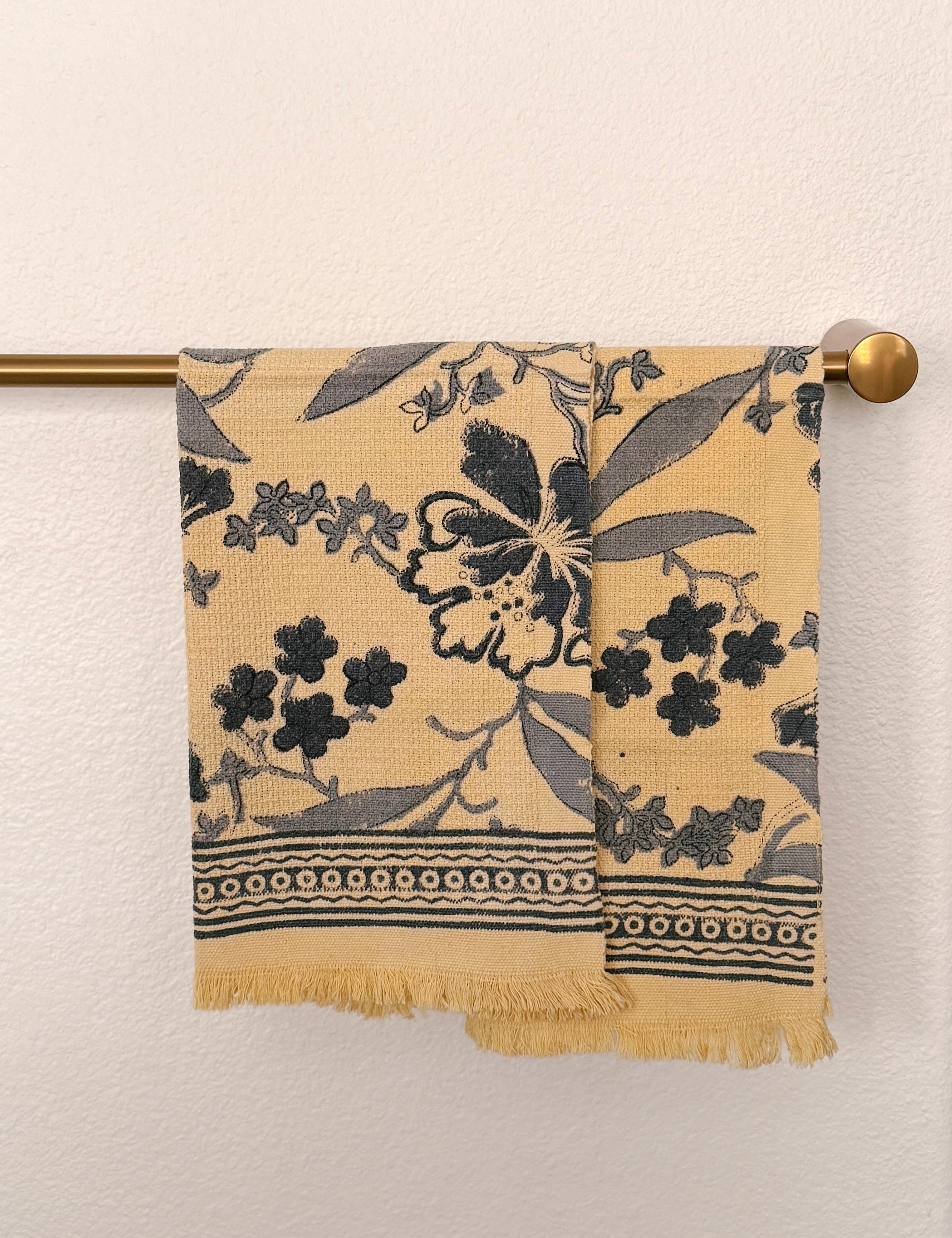 Set of two Bluebell hand block printed Khadi cotton hand towels hanging side-by-side on a brass towel rod featuring slate blue floral vines on a butter-cream background