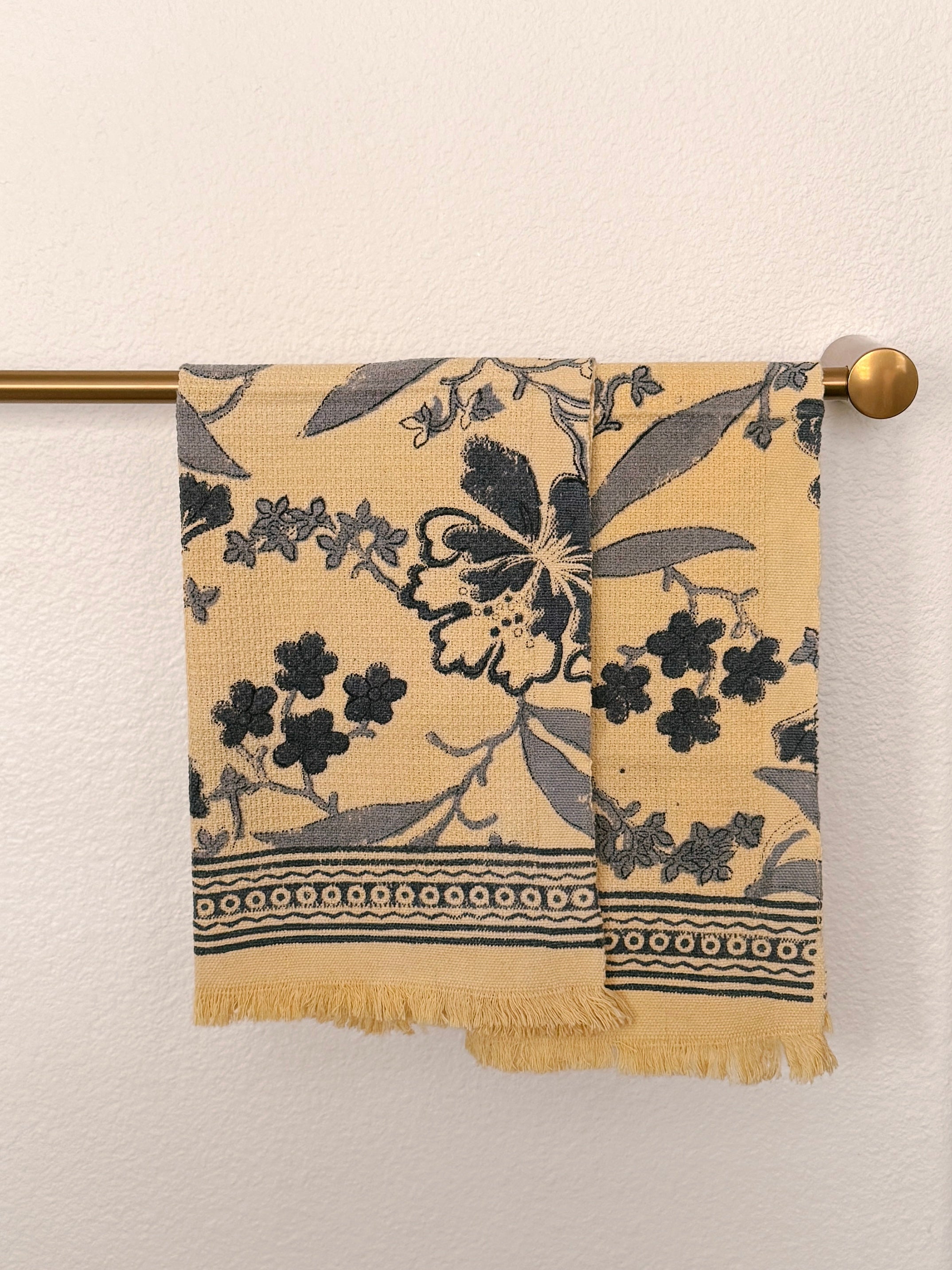 Set of two Bluebell hand block printed Khadi cotton hand towels hanging side-by-side on a brass towel rod featuring slate blue floral vines on a butter-cream background