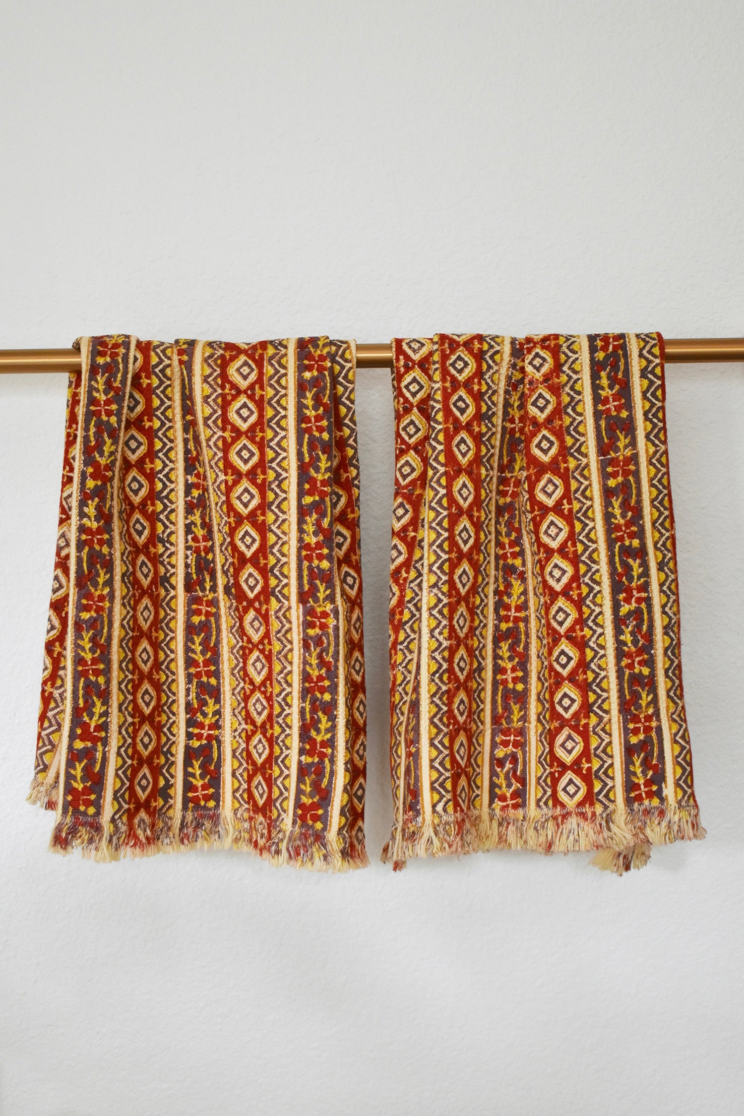 Two Camila block printed khadi cotton hand towels hanging on a gold bathroom rod