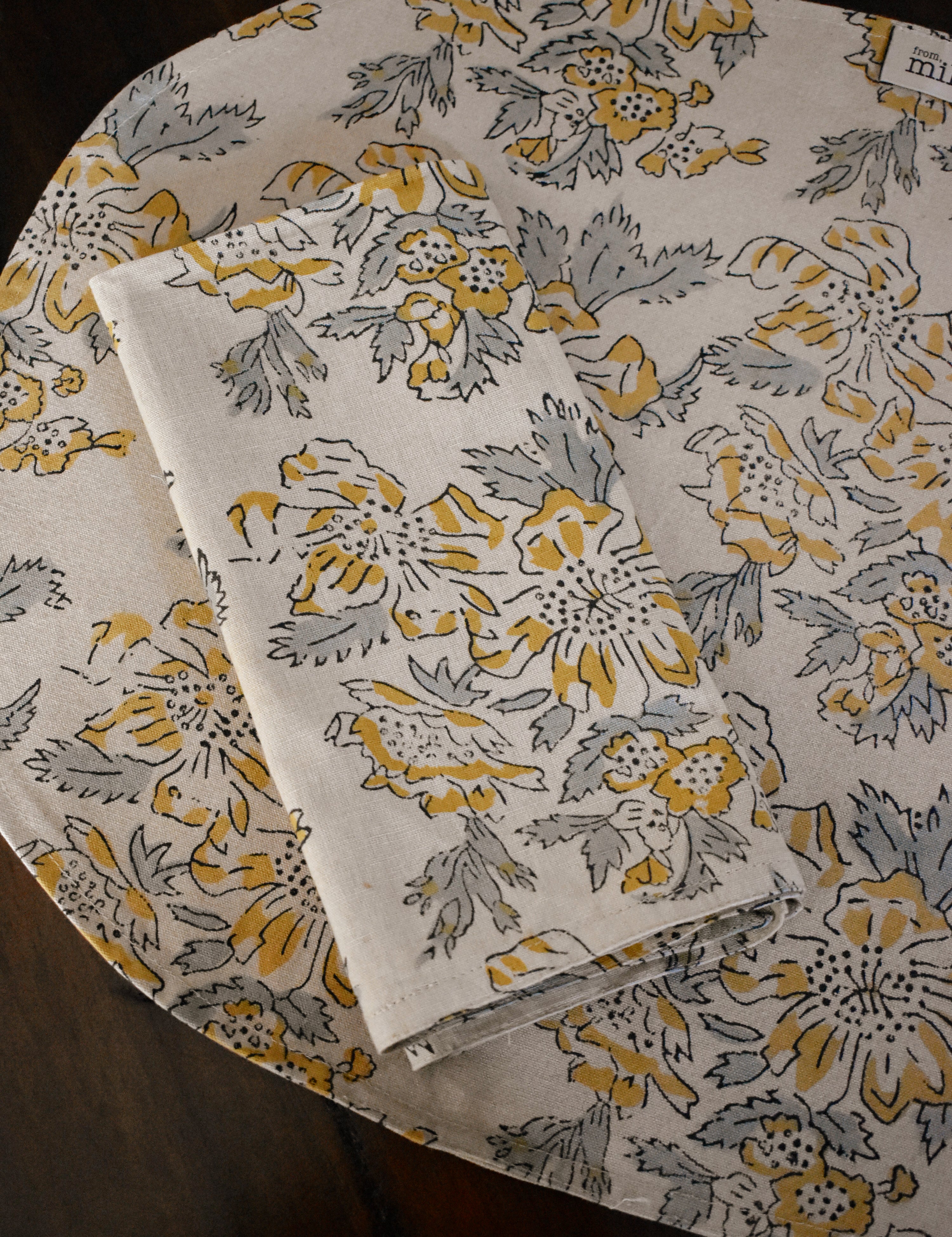 Floral printed placemat with matching table napkin on top, on a wooden surface