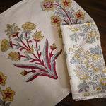 Red, blue and gold floral printed tablecloth and napkin on a wooden surface