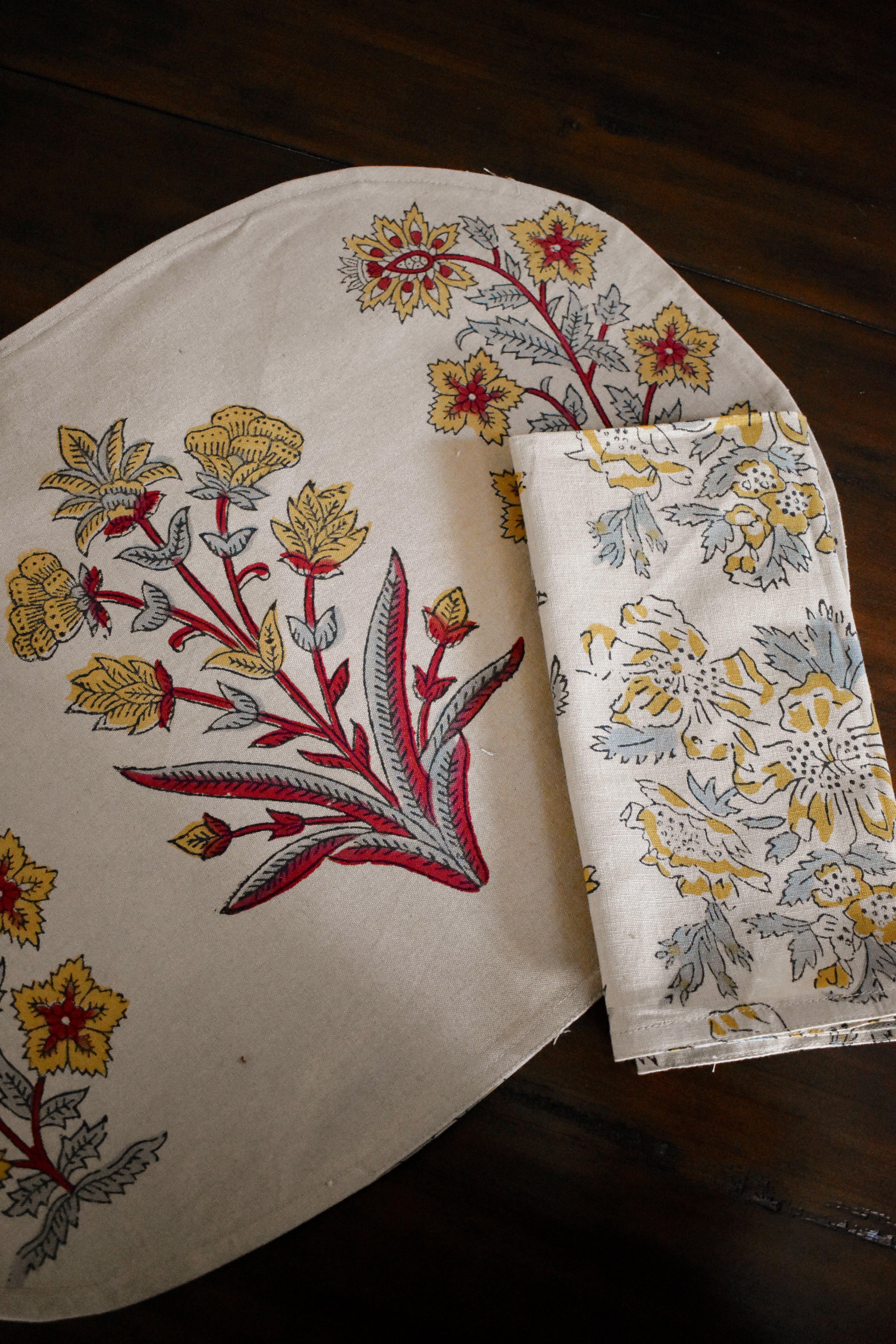 Red, blue and gold floral printed tablecloth and napkin on a wooden surface