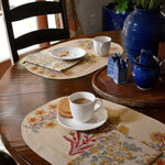 Decorative table setting with floral placemats, cups, and a vase on a wooden table.