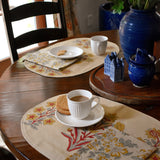 Decorative table setting with floral placemats, cups, and a vase on a wooden table.