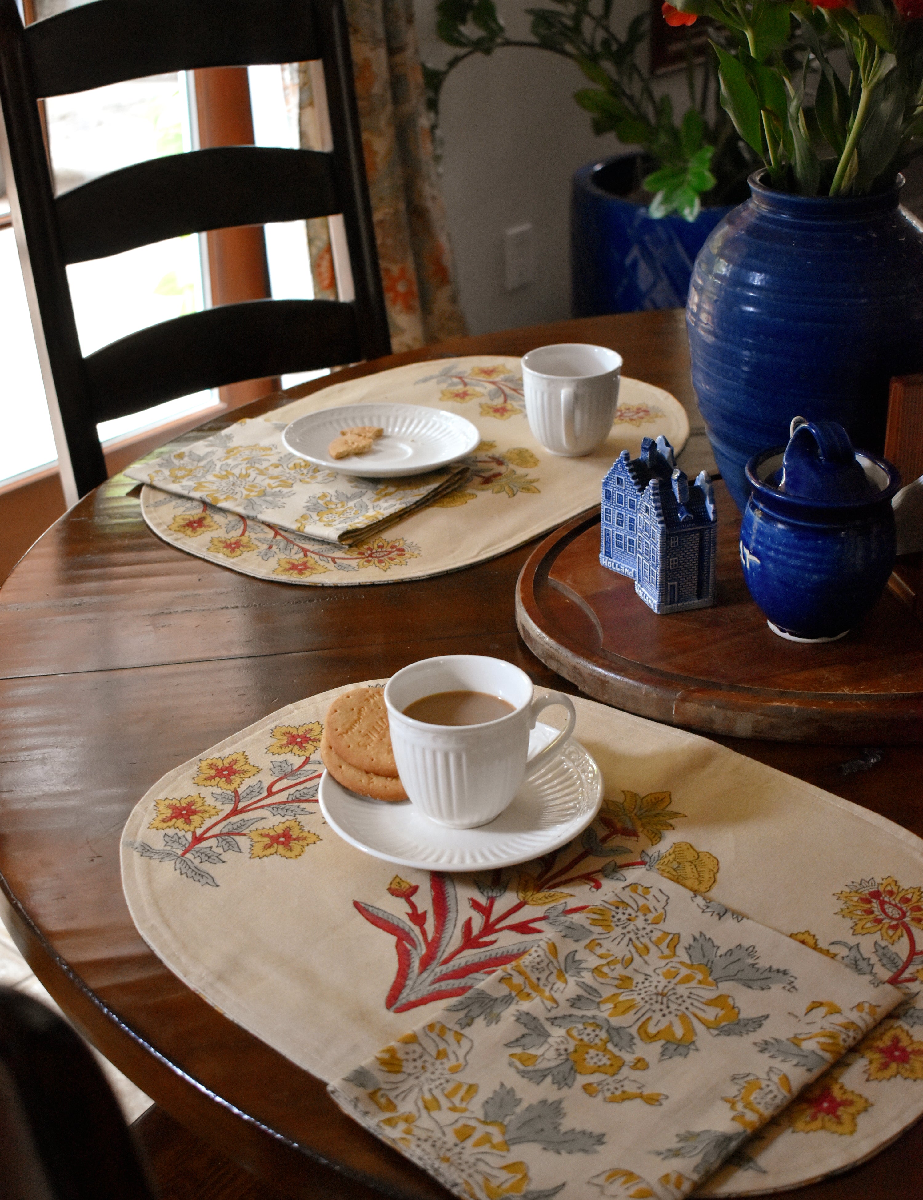 Decorative table setting with floral placemats, cups, and a vase on a wooden table.