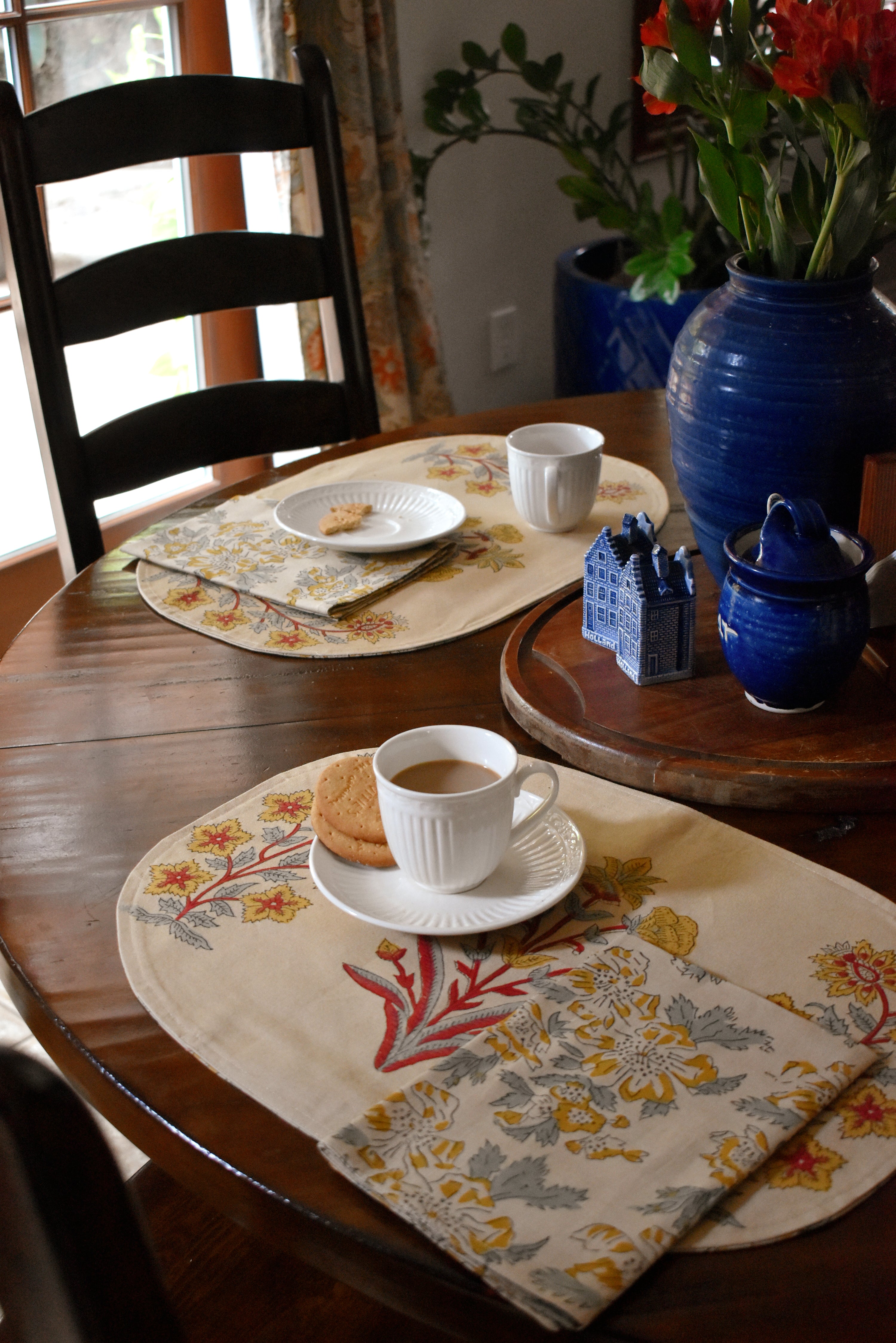 Decorative table setting with floral placemats, cups, and a vase on a wooden table.