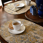 Tablescape with floral printed placemats, table napkins and tea cups, plates, cookies on a wooden table