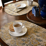 Tablescape with floral printed placemats, table napkins and tea cups, plates, cookies on a wooden table