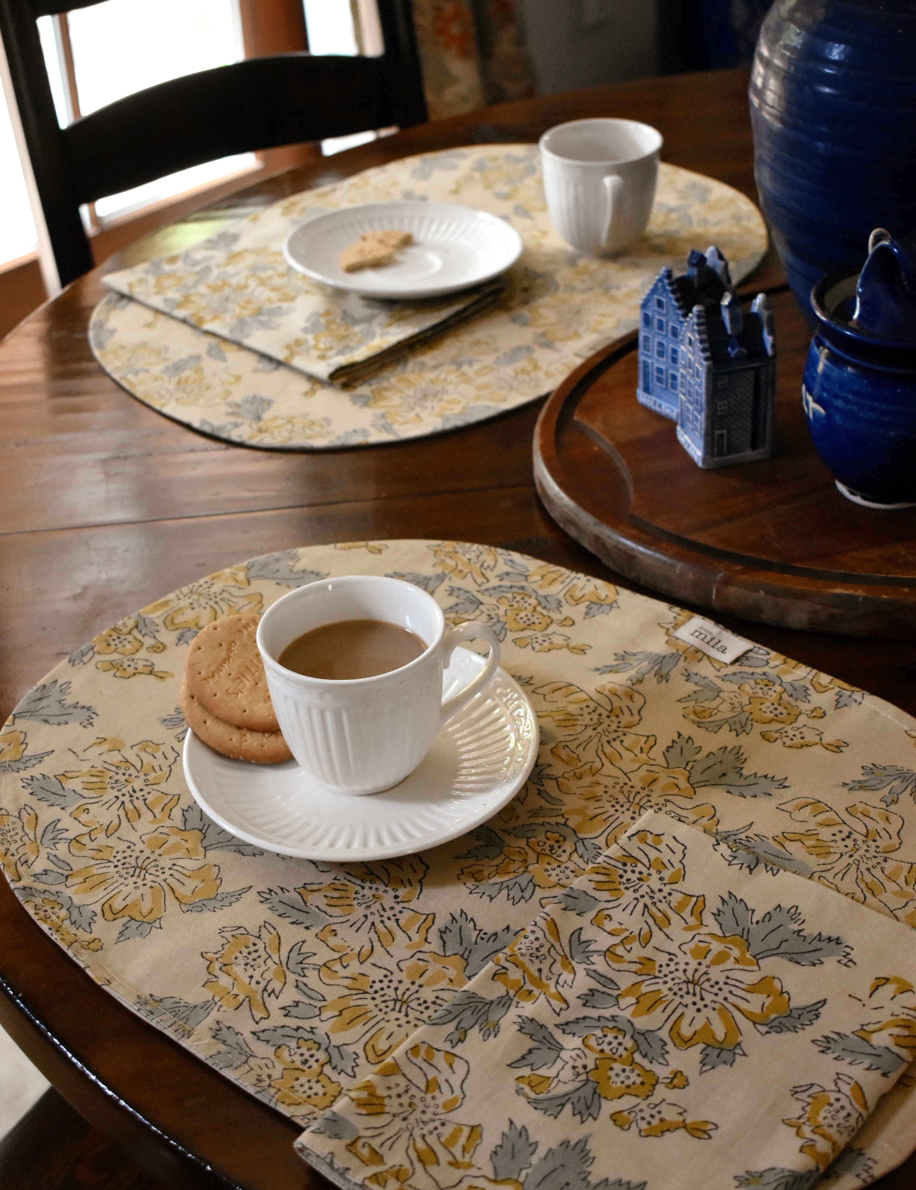Tablescape with floral printed placemats, table napkins and tea cups, plates, cookies on a wooden table