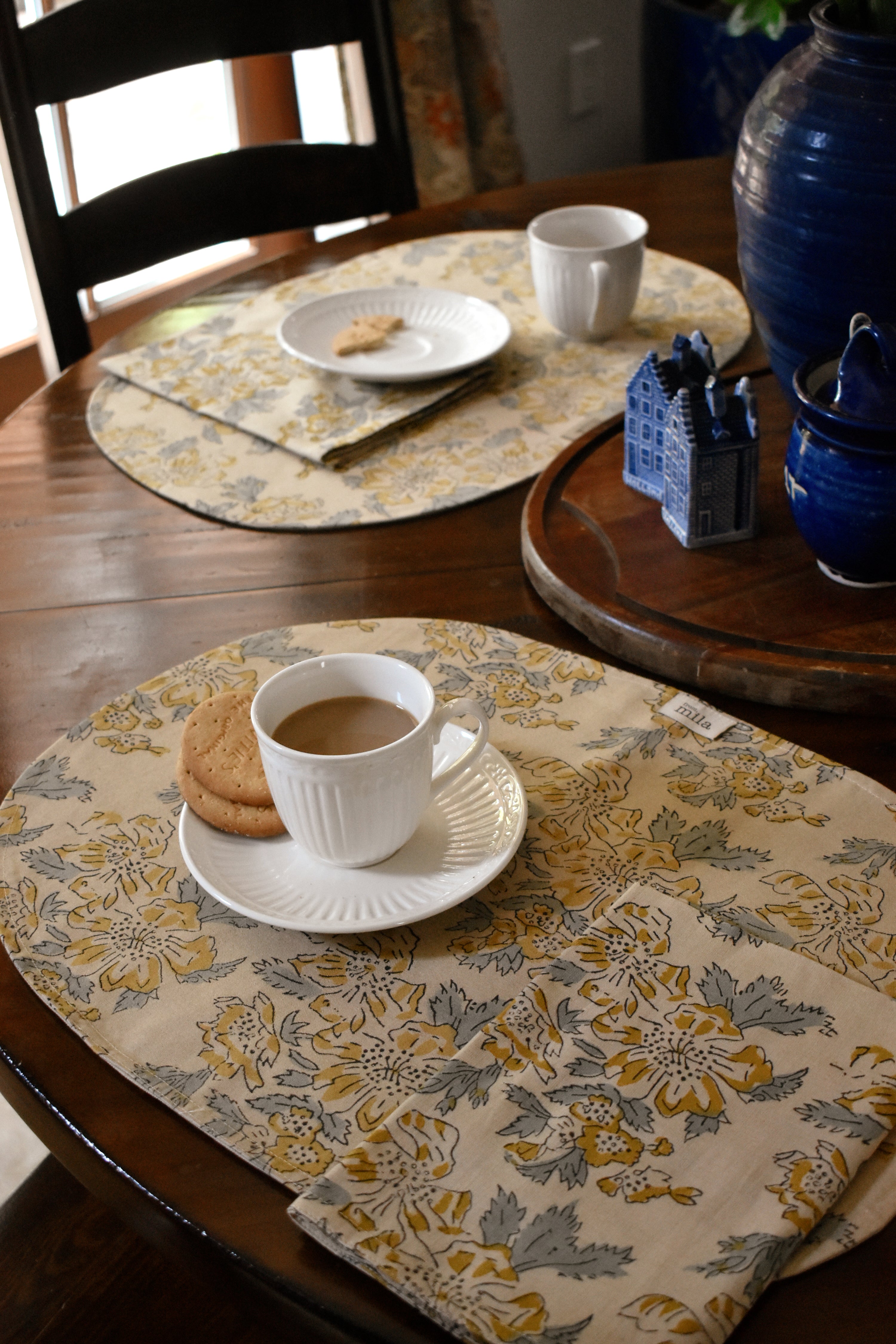 Tablescape with floral printed placemats, table napkins and tea cups, plates, cookies on a wooden table
