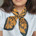 Person wearing a grey shirt with a dark blue and gold floral printed bandana scarf around their neck.
