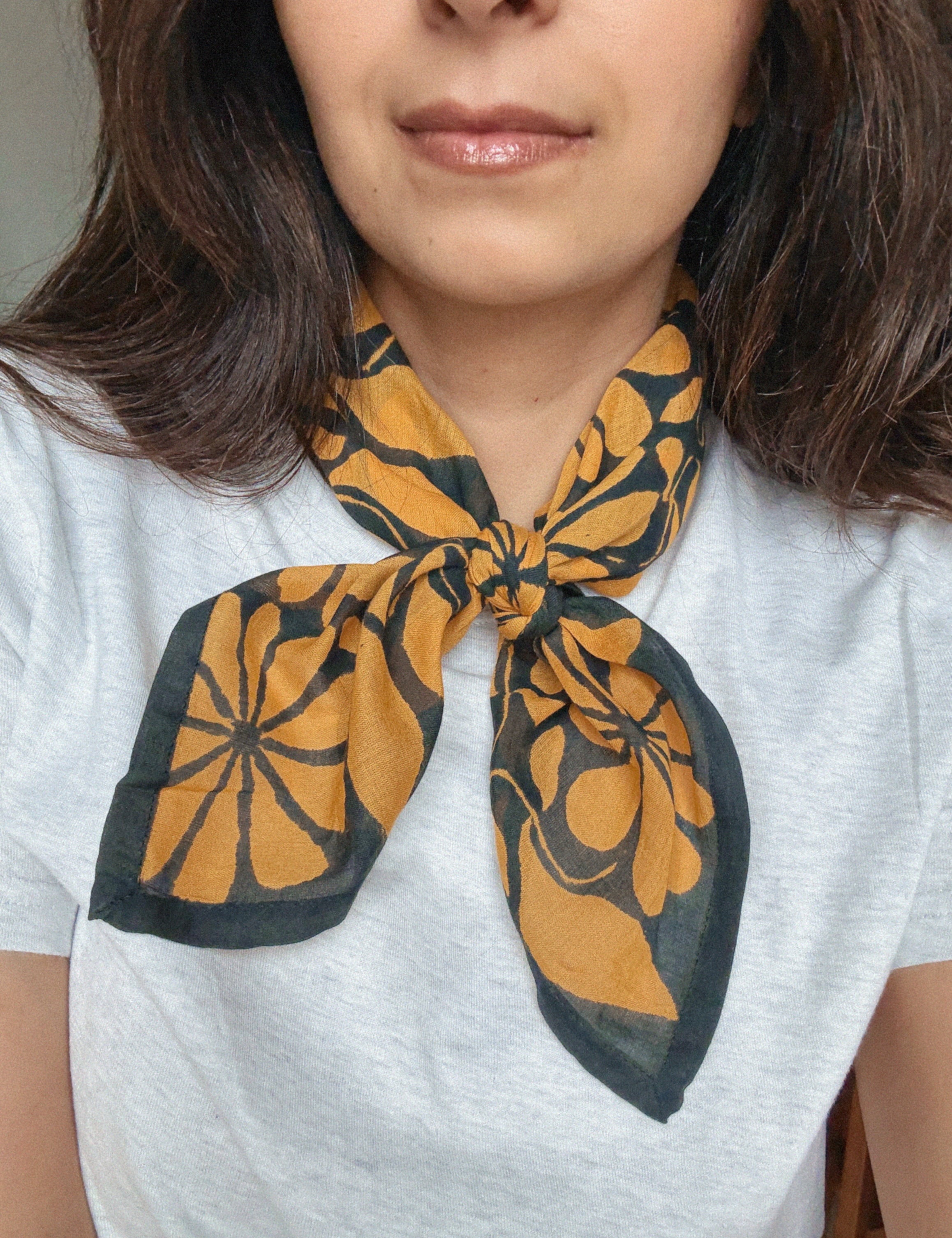 Person wearing a grey shirt with a dark blue and gold floral printed bandana scarf around their neck.