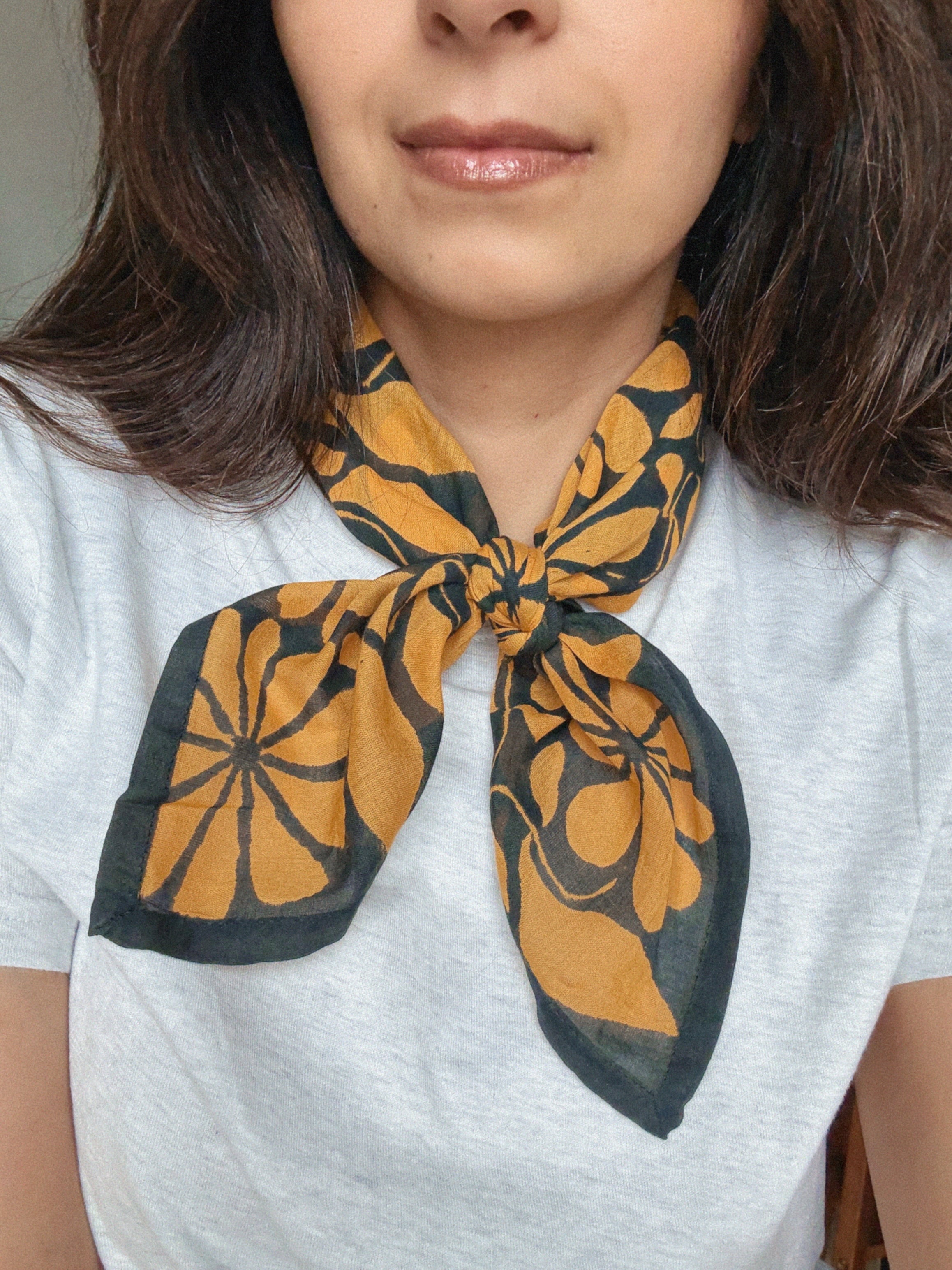 Person wearing a grey shirt with a dark blue and gold floral printed bandana scarf around their neck.