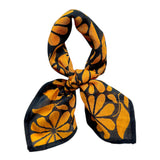 Chai bandana scarf tied on white background. Scarf has a blueish black background and large golden floral print allover.