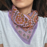 Person wearing a colorful lavender floral patterned bandana scarf on a grey t shirt