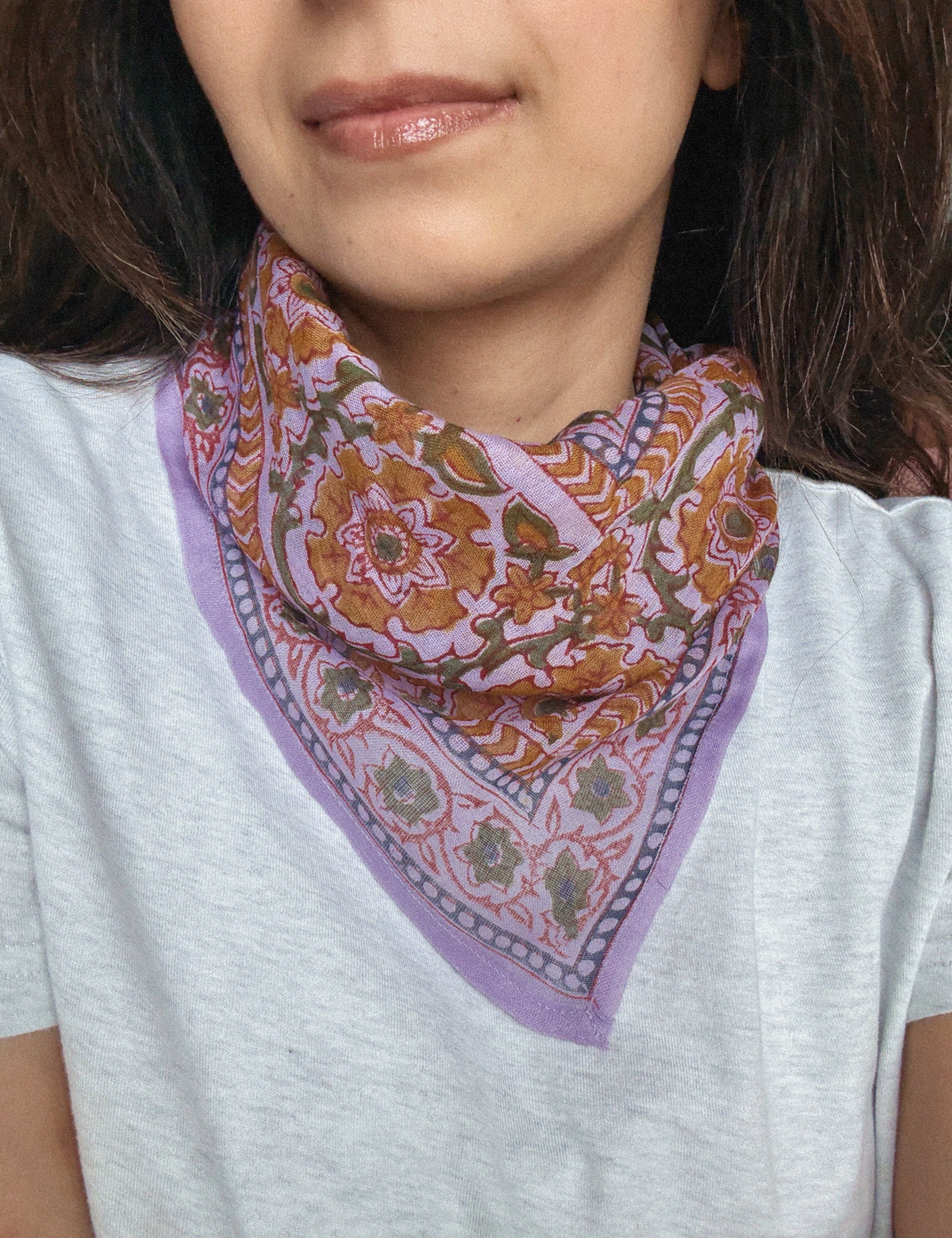Person wearing a colorful lavender floral patterned bandana scarf on a grey t shirt