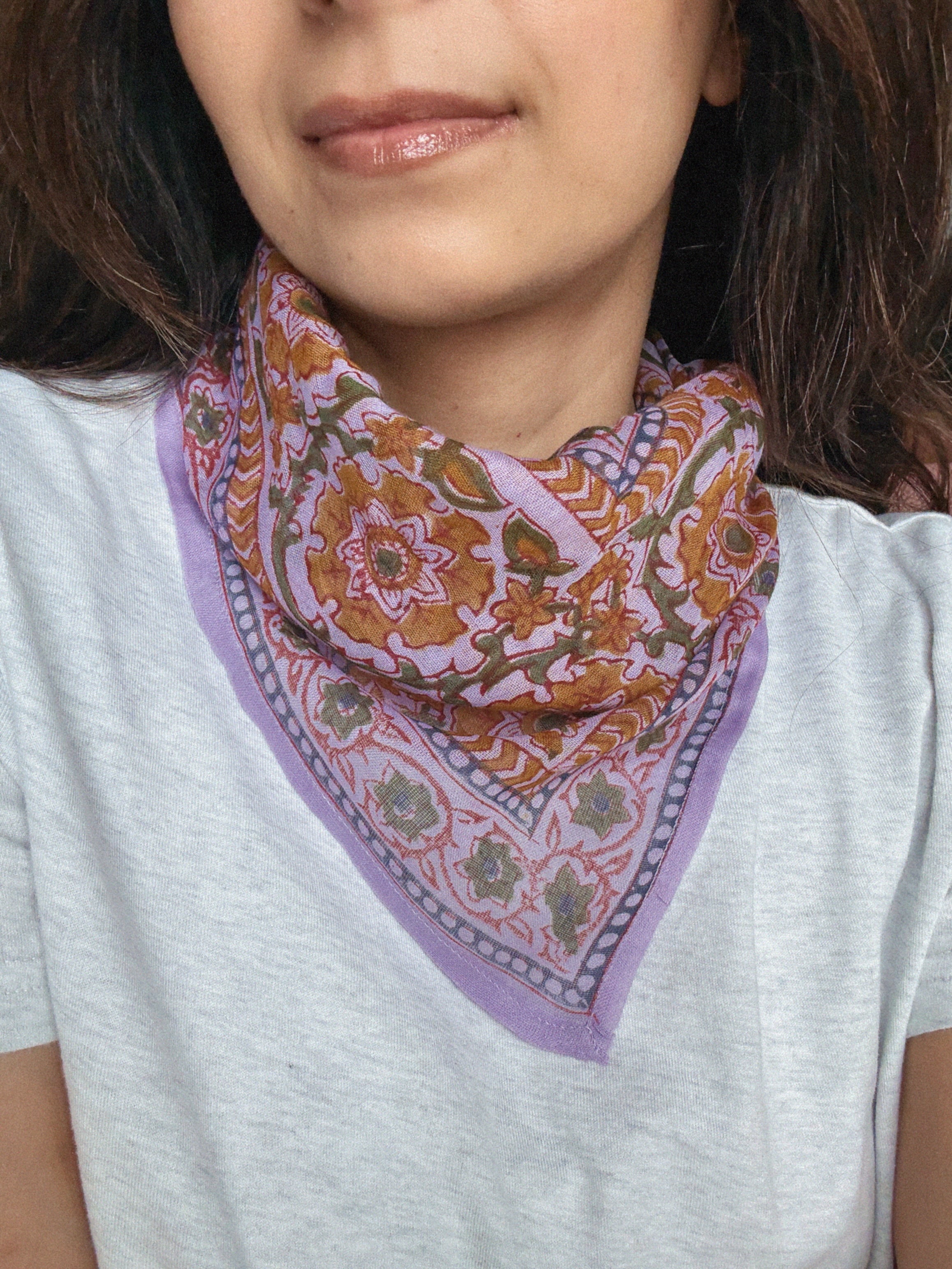 Person wearing a colorful lavender floral patterned bandana scarf on a grey t shirt