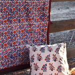 Floral printed blanket draped over a wooden fence in a rustic setting. Floral printed pillows sitting on ground in front of blanket.