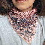 Person wearing a block printed patterned bandana scarf on a grey tee shirt. Scarf has a floral print in red and blue