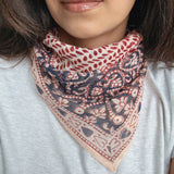 Person wearing a block printed patterned bandana scarf on a grey tee shirt. Scarf has a floral print in red and blue