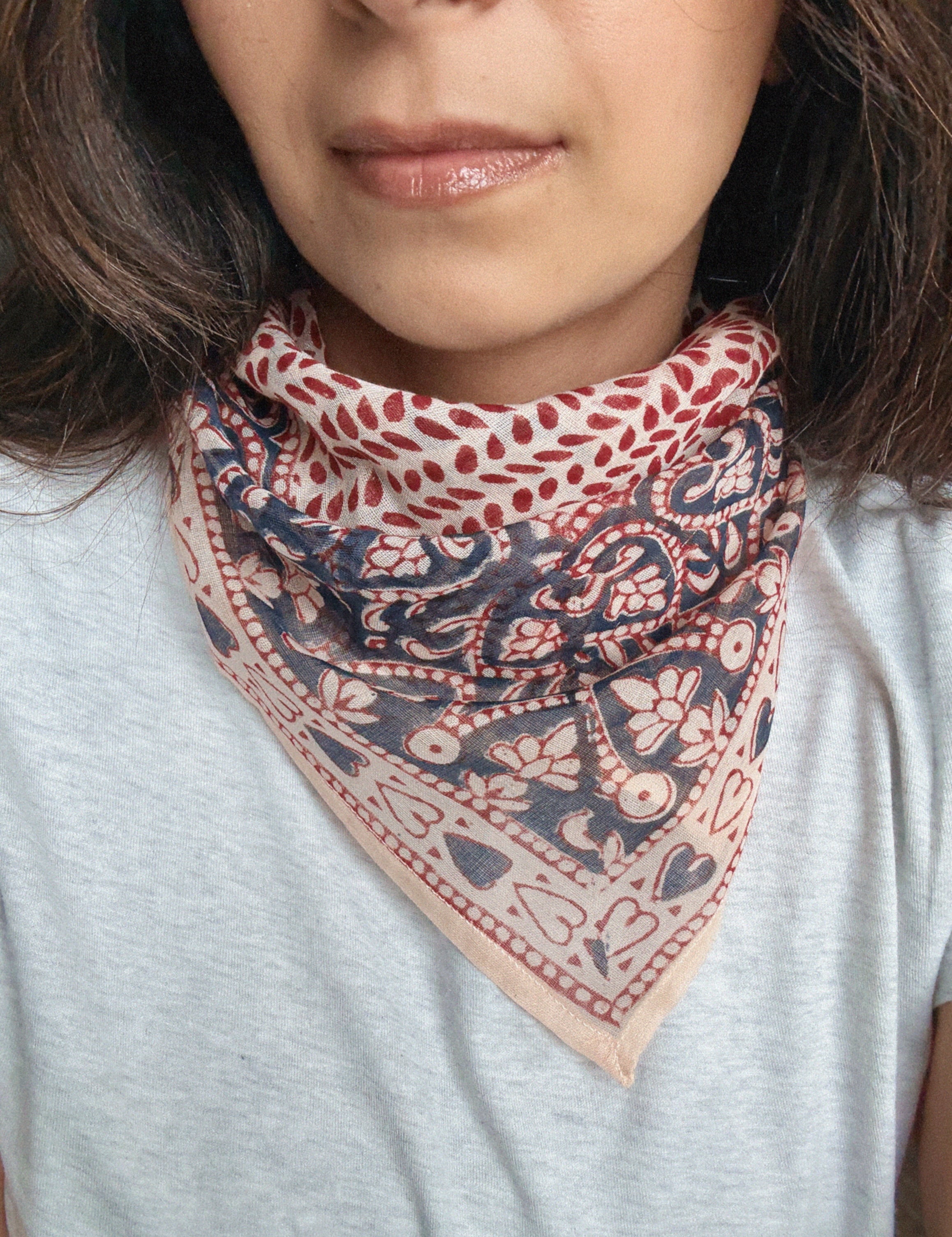 Person wearing a block printed patterned bandana scarf on a grey tee shirt. Scarf has a floral print in red and blue