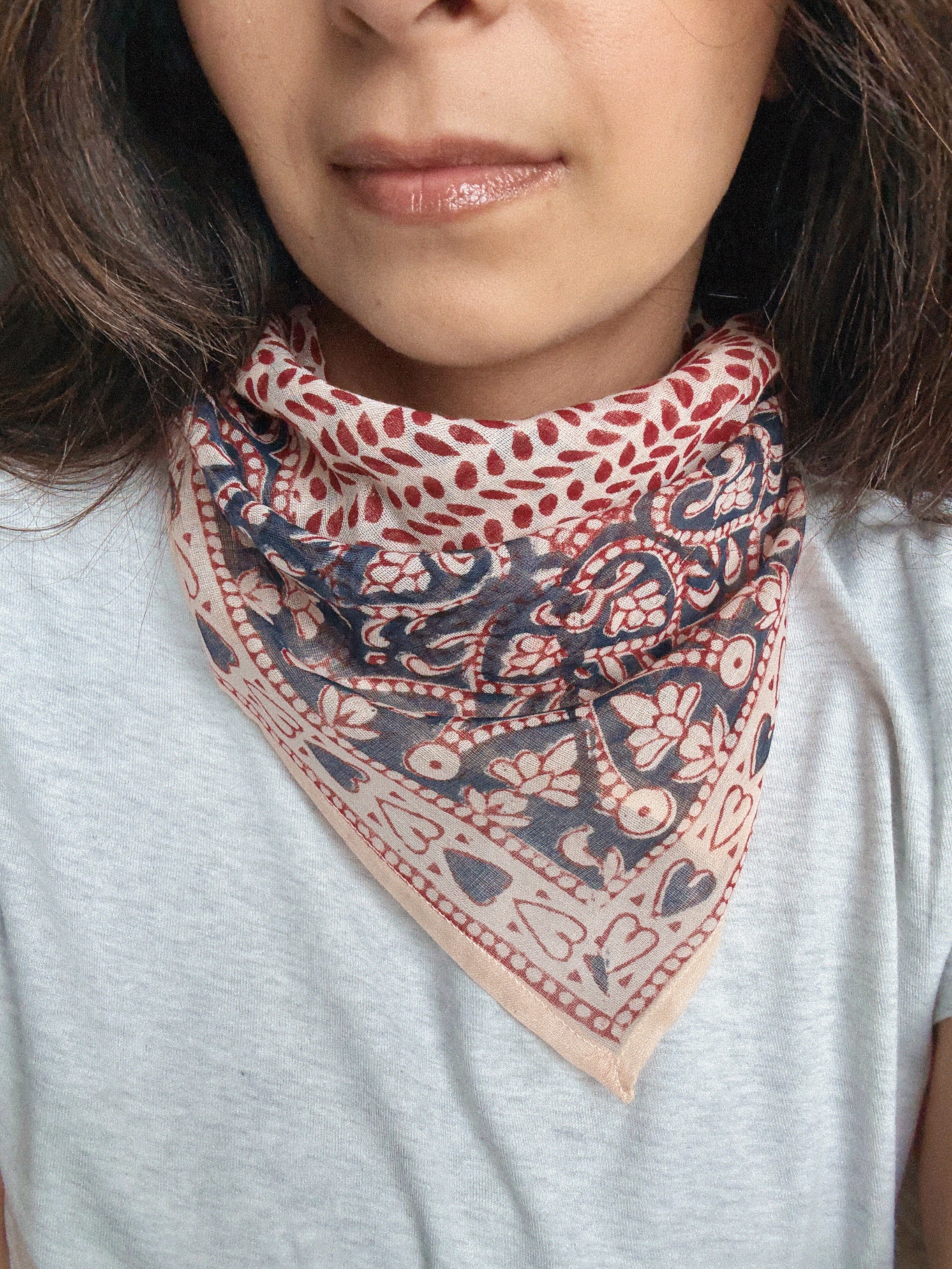 Person wearing a block printed patterned bandana scarf on a grey tee shirt. Scarf has a floral print in red and blue