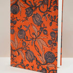 Book with black floral pattern on an orange cover against a beige background