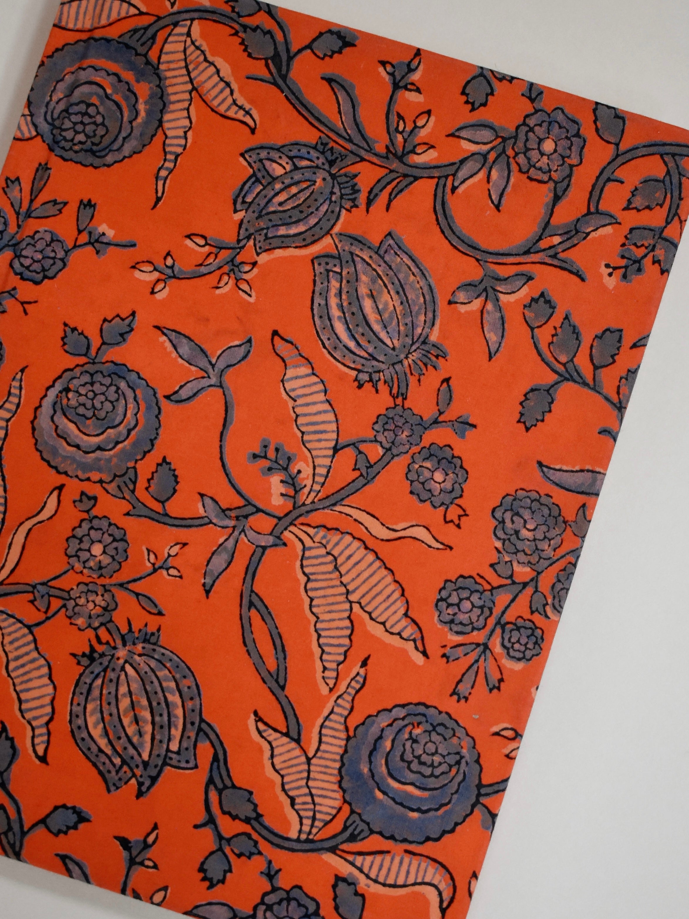 Orange journal with navy floral print on beige background, laid flat, angled shot