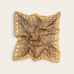 A square scarf with an intricate paisley and floral pattern in sage and gold, laid flat on a light beige background.