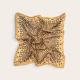 A square scarf with an intricate paisley and floral pattern in sage and gold, laid flat on a light beige background.
