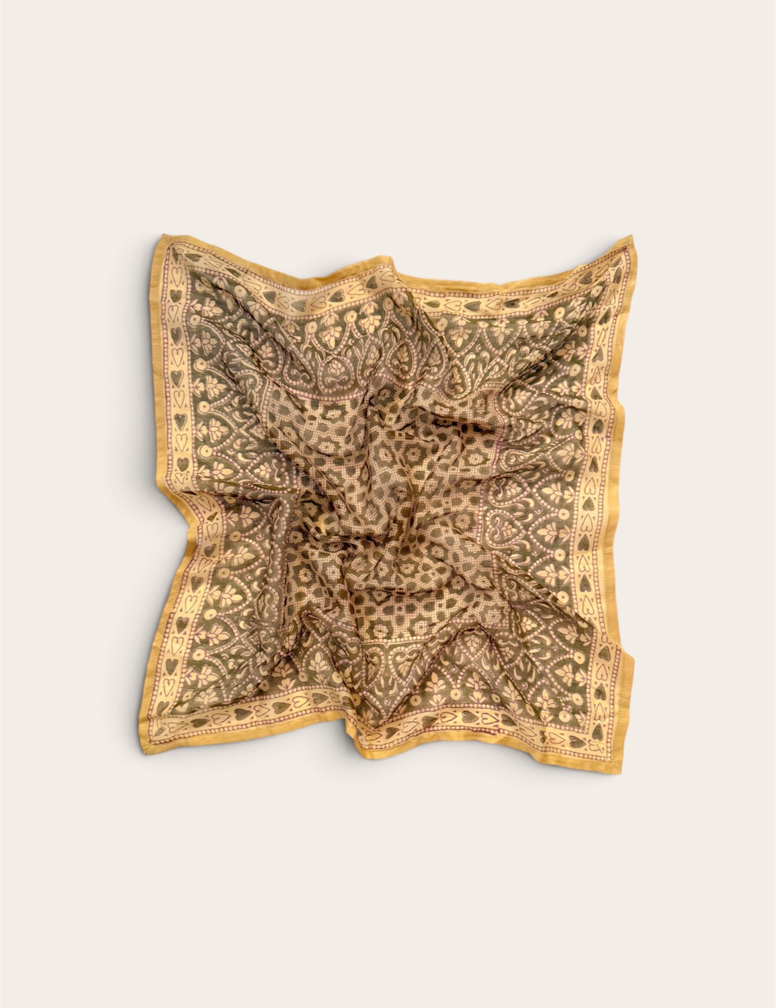 A square scarf with an intricate paisley and floral pattern in sage and gold, laid flat on a light beige background.