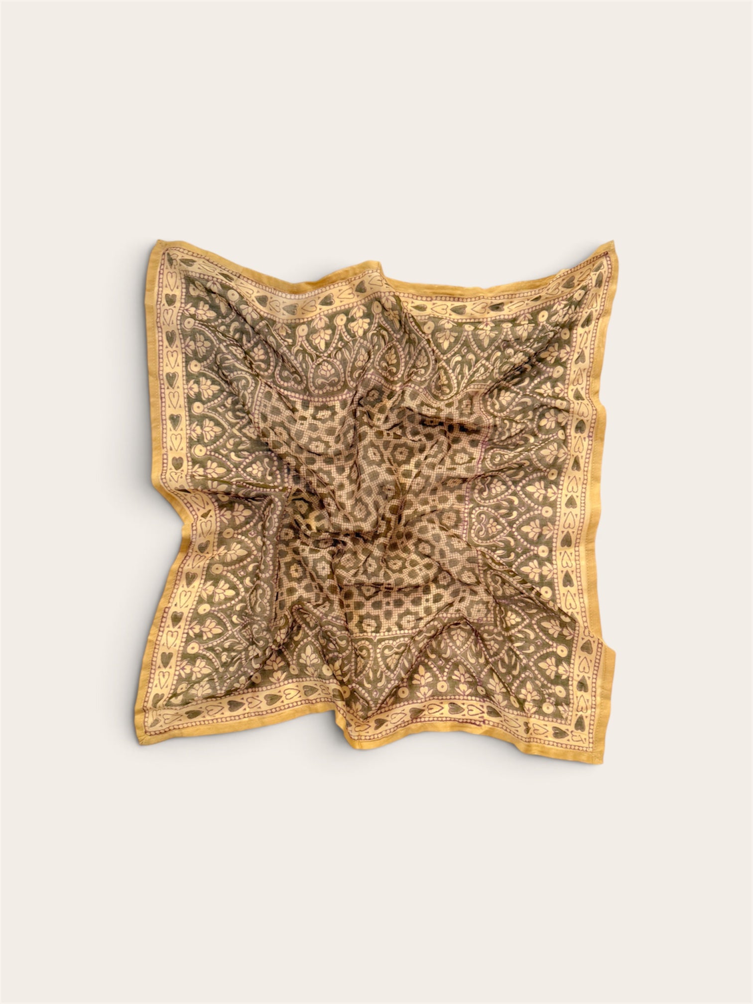 A square scarf with an intricate paisley and floral pattern in sage and gold, laid flat on a light beige background.