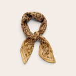 A small patterned scarf tied in a knot, displayed against a plain light beige background. The scarf features a warm sage and gold paisley pattern with muted accents.
