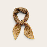 A small patterned scarf tied in a knot, displayed against a plain light beige background. The scarf features a warm sage and gold paisley pattern with muted accents.