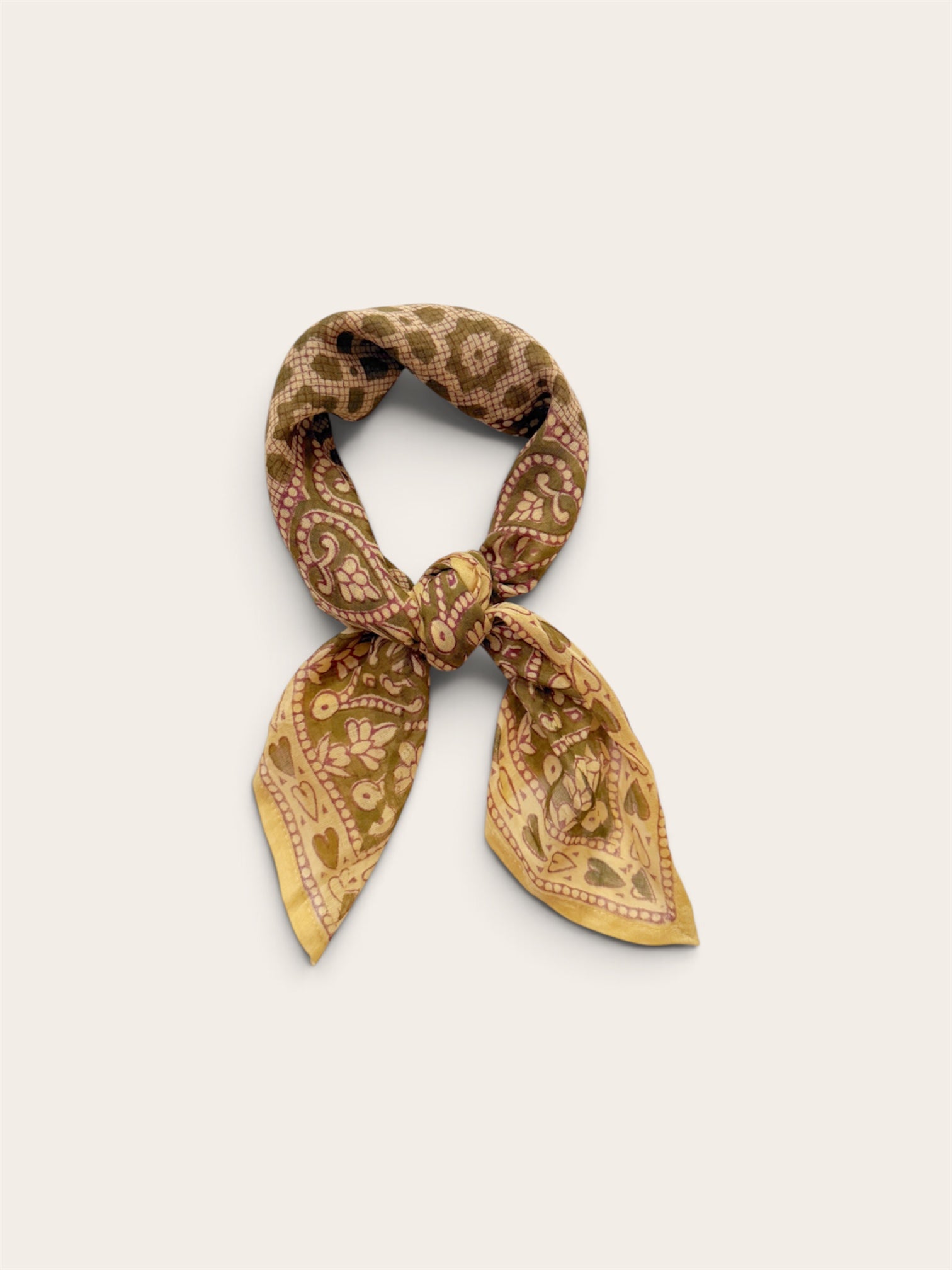 A small patterned scarf tied in a knot, displayed against a plain light beige background. The scarf features a warm sage and gold paisley pattern with muted accents.