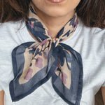 Person wearing a block printed patterned bandana scarf on a grey tee shirt. Scarf has a floral print in blue and lavender