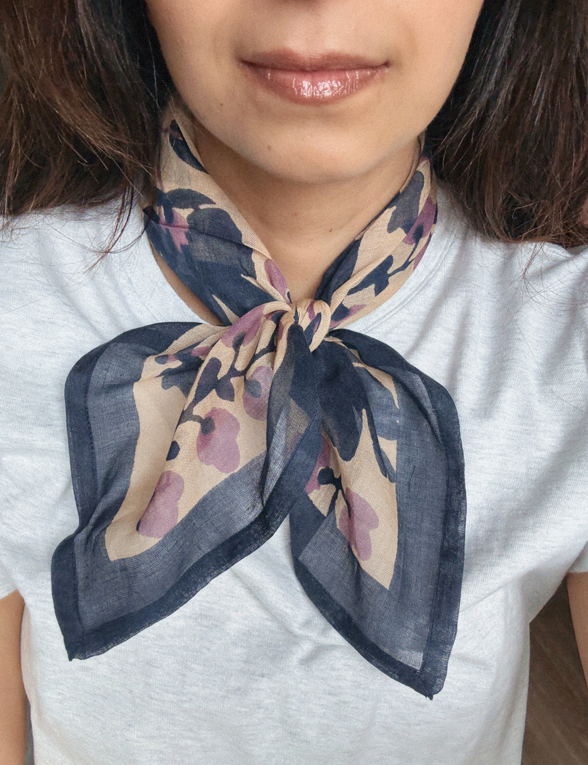 Person wearing a block printed patterned bandana scarf on a grey tee shirt. Scarf has a floral print in blue and lavender