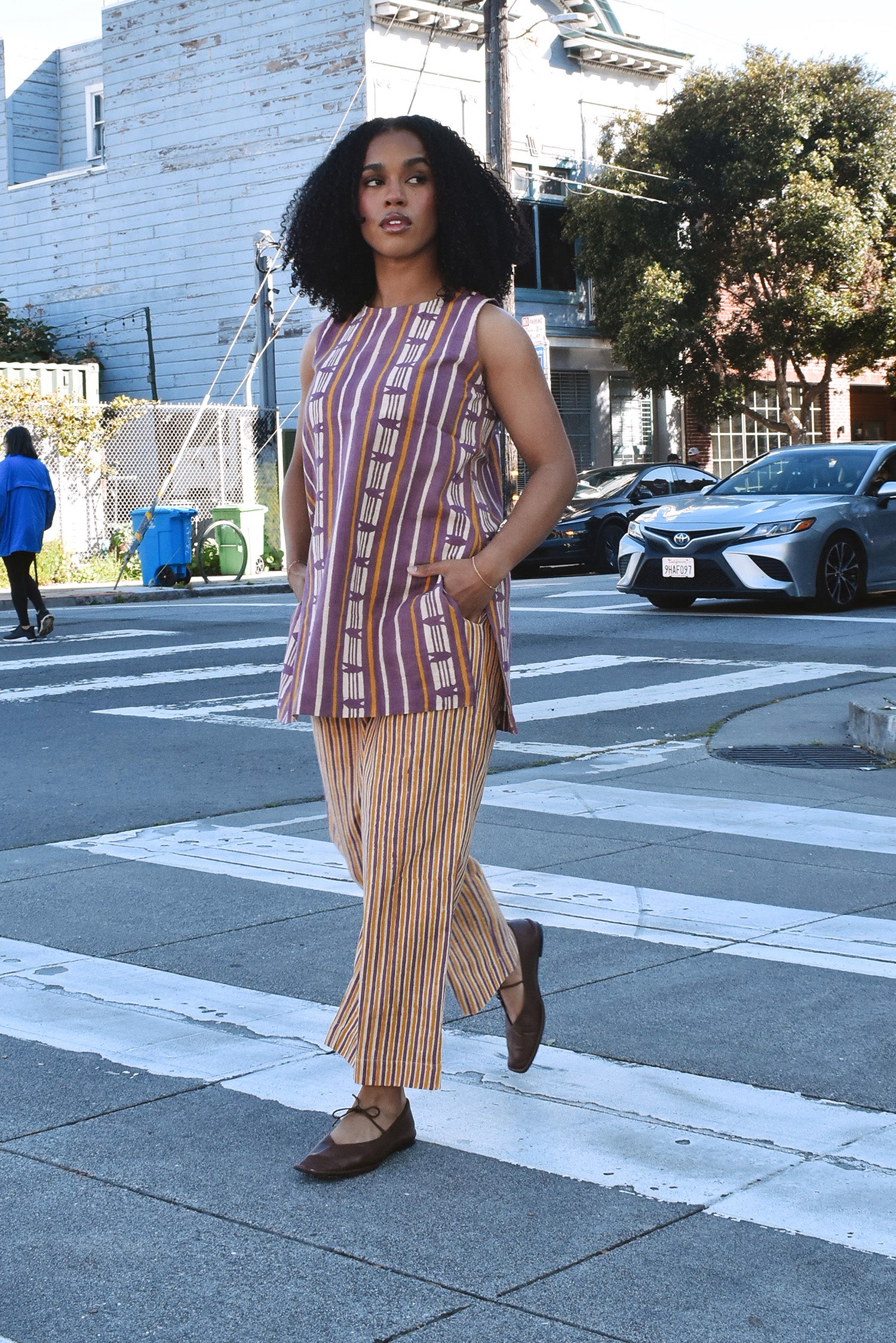 Woman in a striped sleeveless top and cropped pant set outfit crossing a street in an urban setting