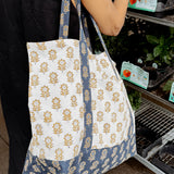 Woman wearing blue and gold floral printed tote bag outside while picking plants
