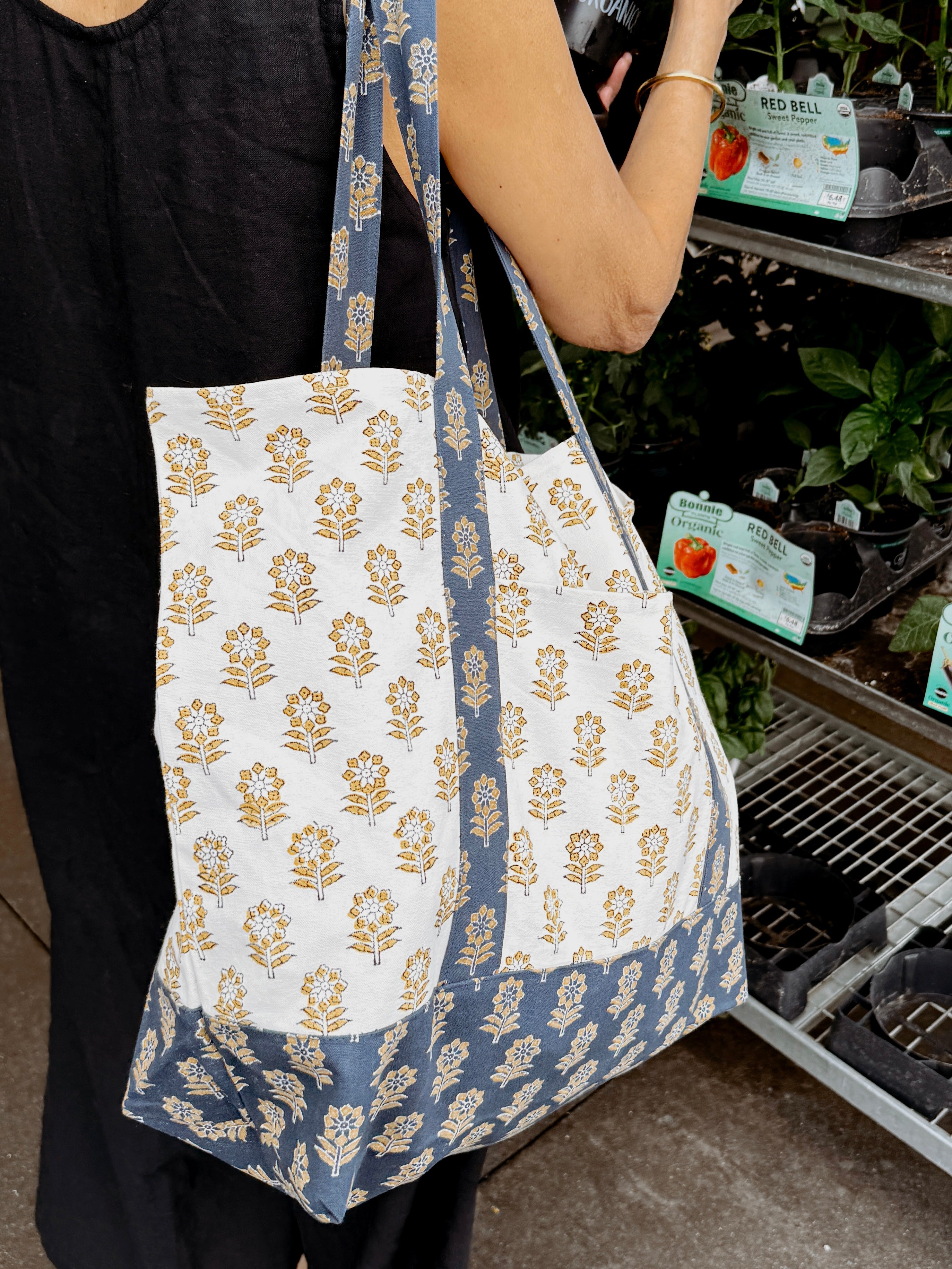 Woman wearing blue and gold floral printed tote bag outside while picking plants