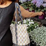 Woman wearing blue and gold floral printed tote bag while picking out flowers